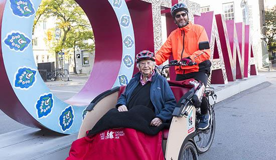 an older adult sits in a carriage being pushed by a bike