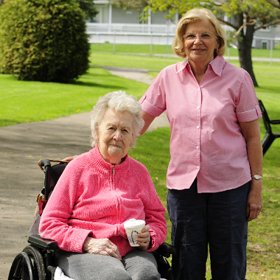 A woman stands by a resident in a wheelchair.